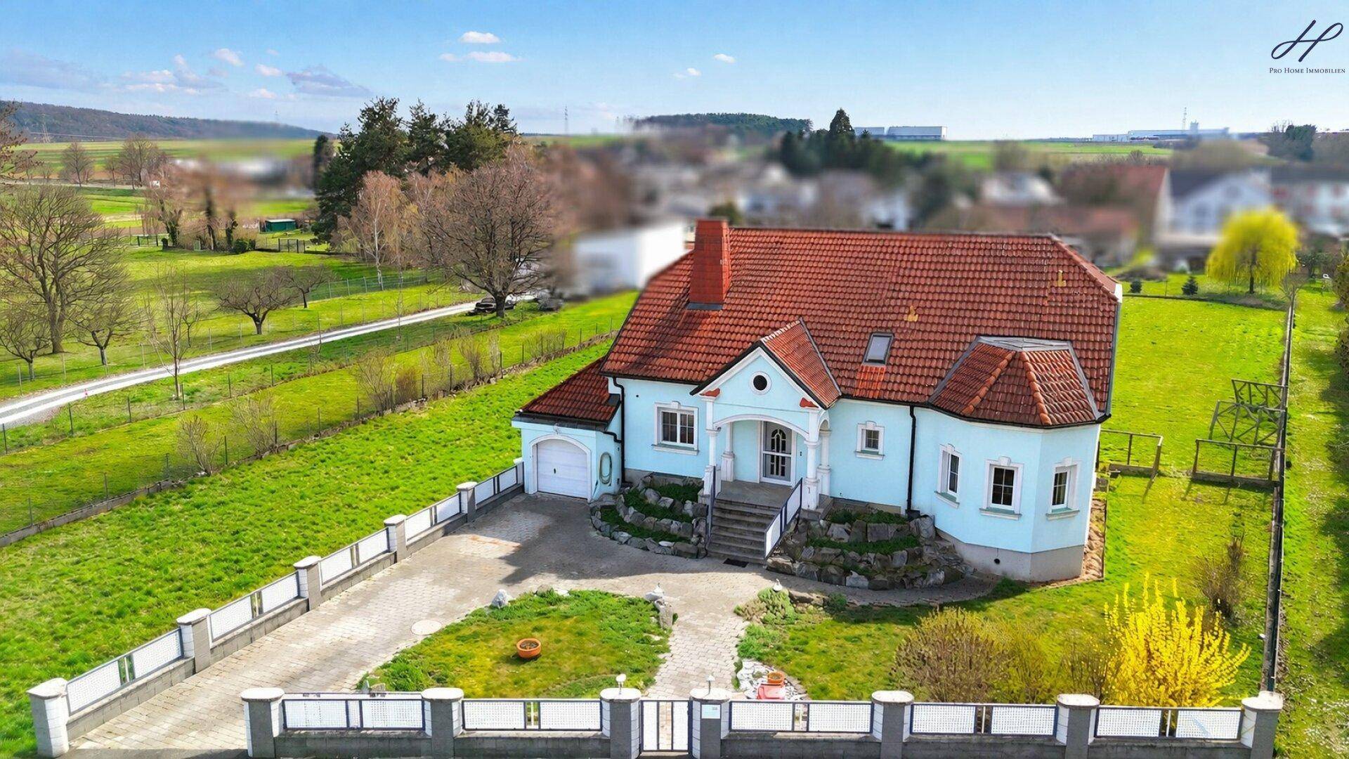 Weitläufige Ansicht eines Einfamilienhauses mit großem Garten und ländlichem Panorama unter blauem Himmel.