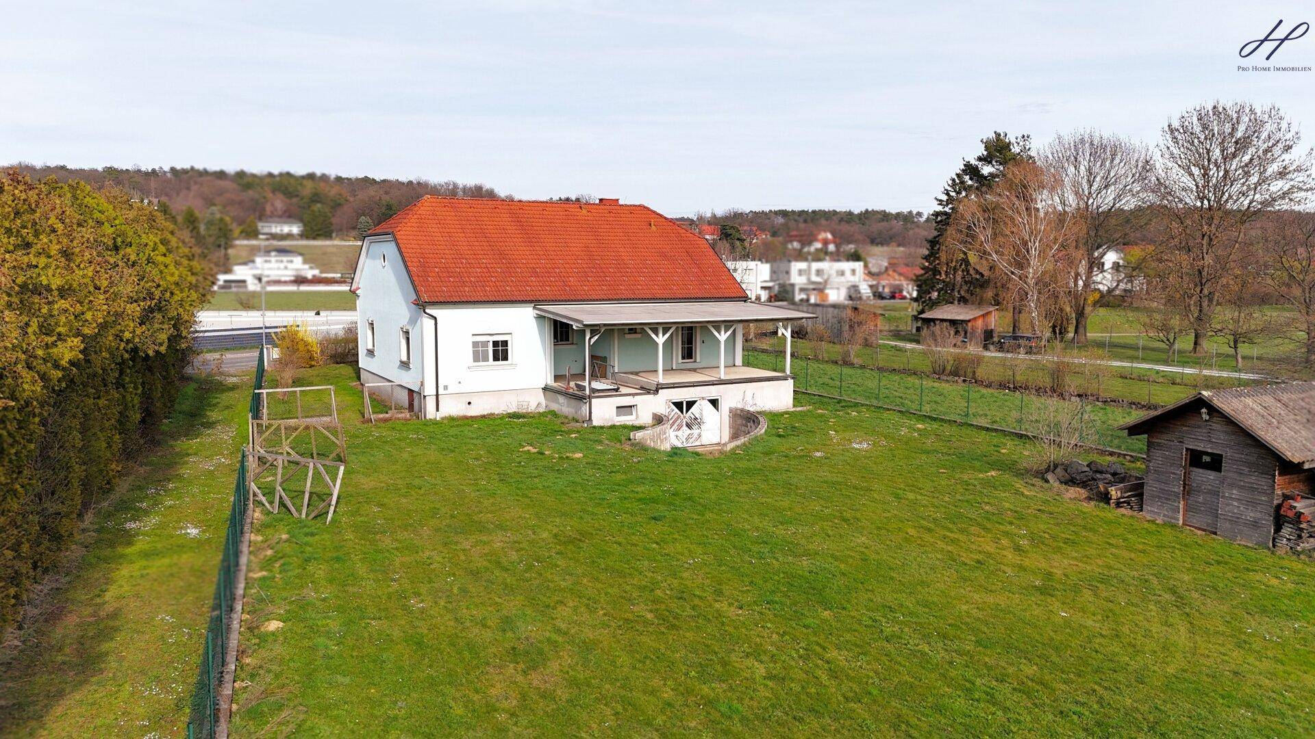 Rückansicht des Hauses mit überdachter Terrasse und großem, unmöbliertem Gartenbereich.
