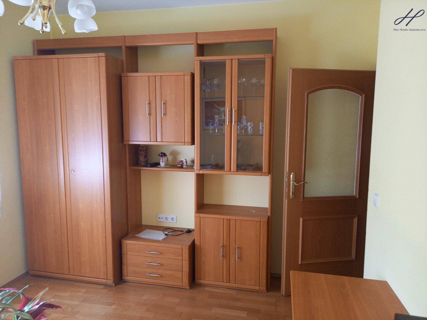 Wohnzimmer mit großer Holzschrankwand und Zugang zu einem weiteren Raum.