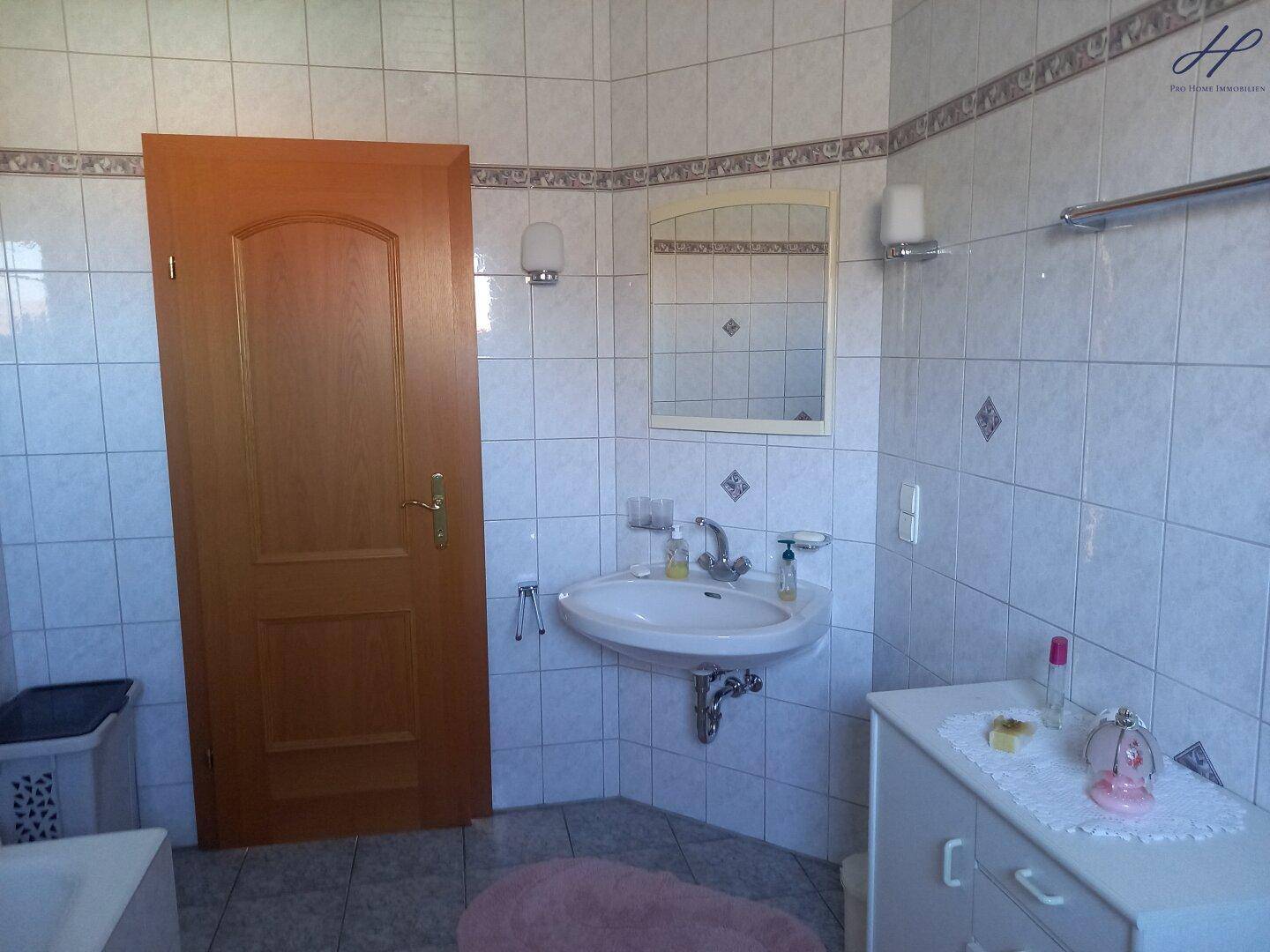 Badezimmer mit Waschbecken, Spiegelschrank und hellen Fliesen.