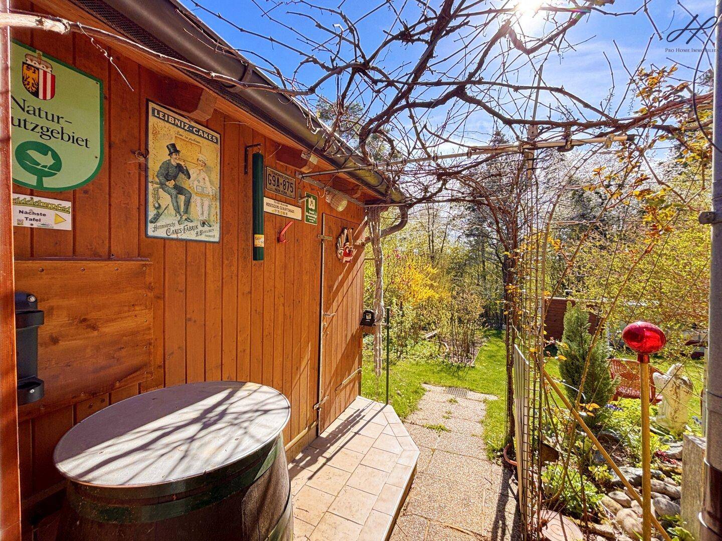 Hölzerner Schuppen mit Rankpflanzen und einem Weg, der in den grünen Garten führt.