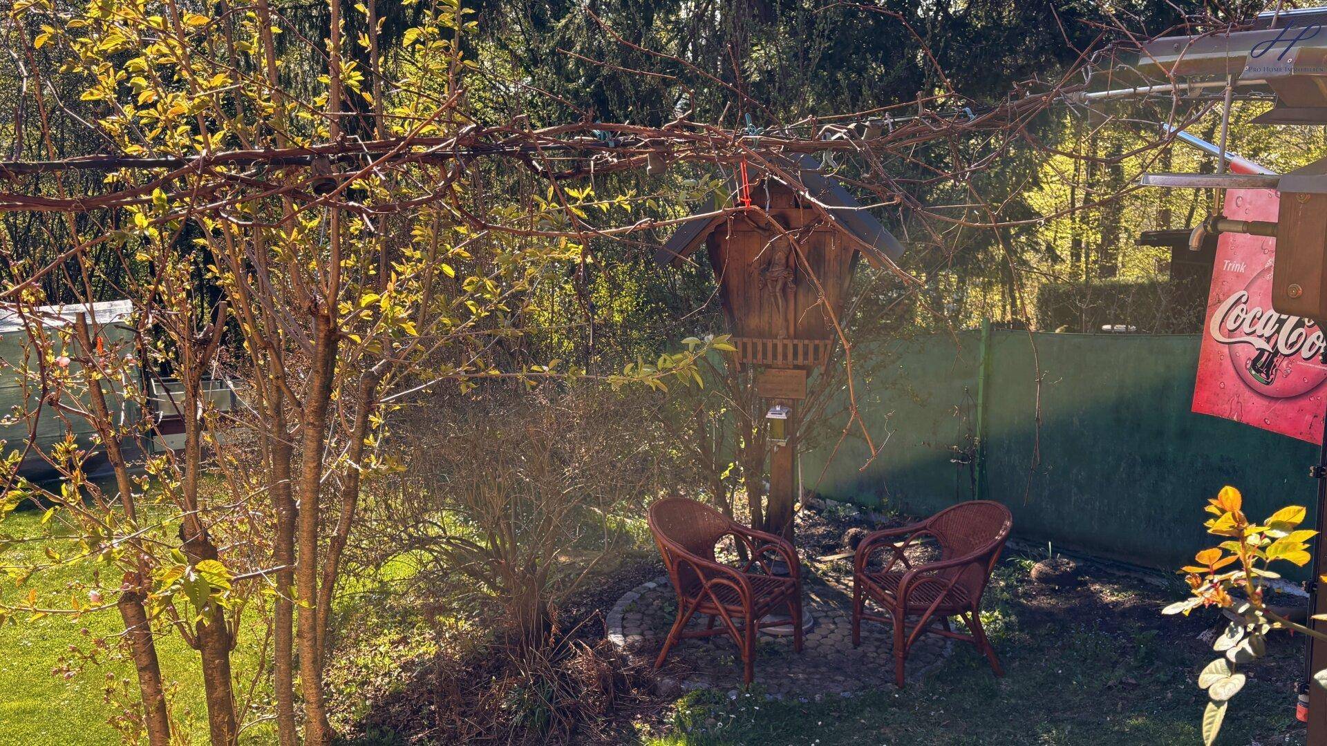 Gemütlicher Gartenbereich mit Korbsesseln, Vogelhaus und üppiger Vegetation.