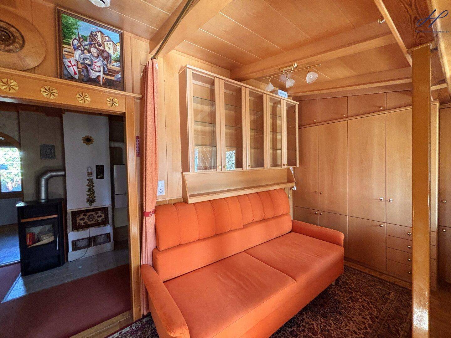 Gemütlicher Wohnbereich mit Holzdecke, orangefarbenem Sofa und Einbauschränken.