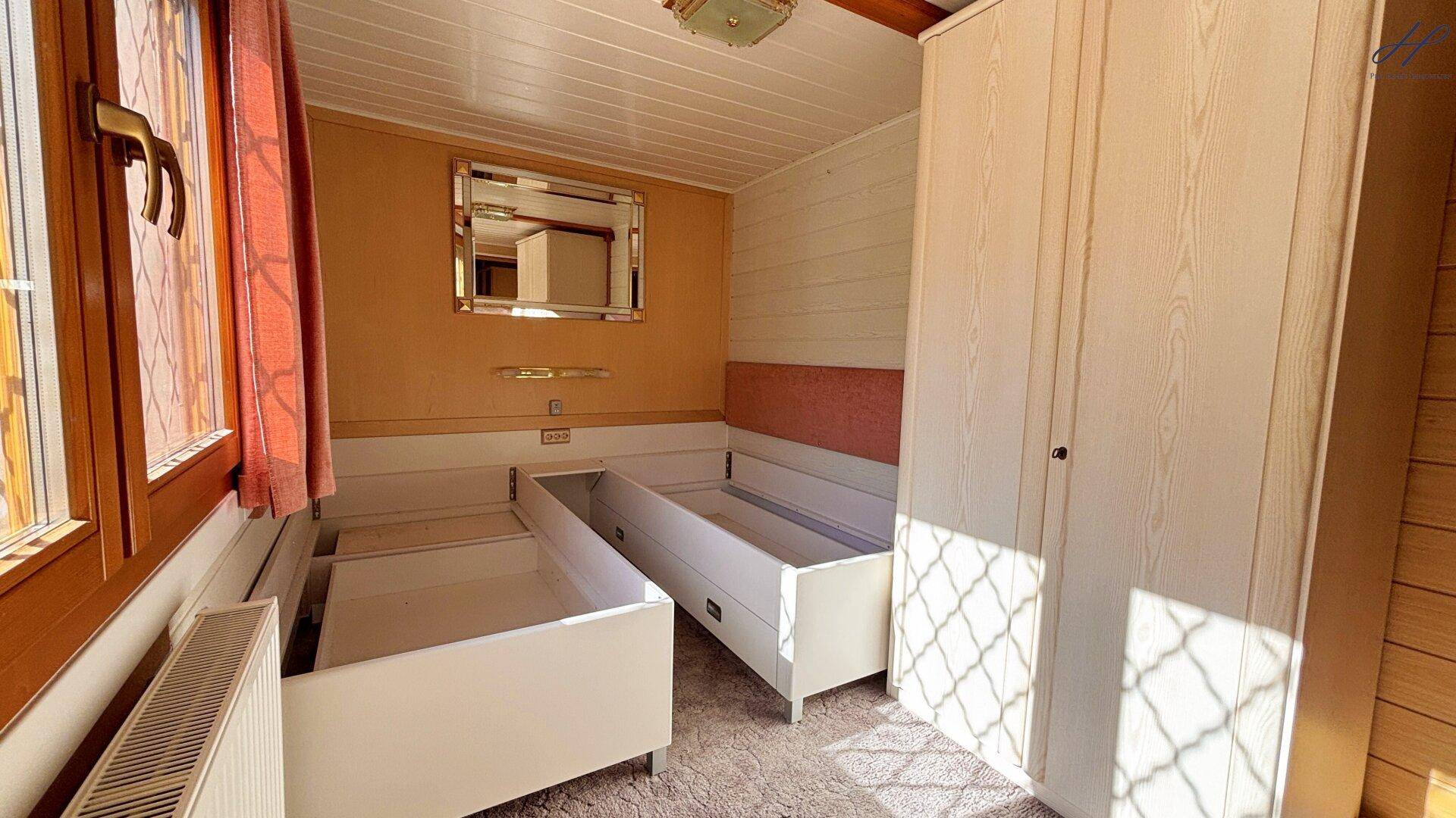 Schlafzimmer mit zwei Einzelbetten, weißem Kleiderschrank und Holzverkleidung.