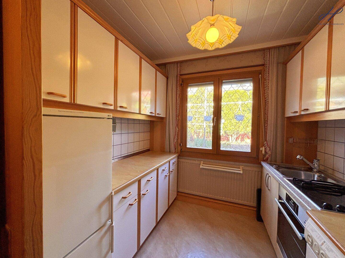Funktionale Küche mit weißen Schränken, Holztheke und Fenster.