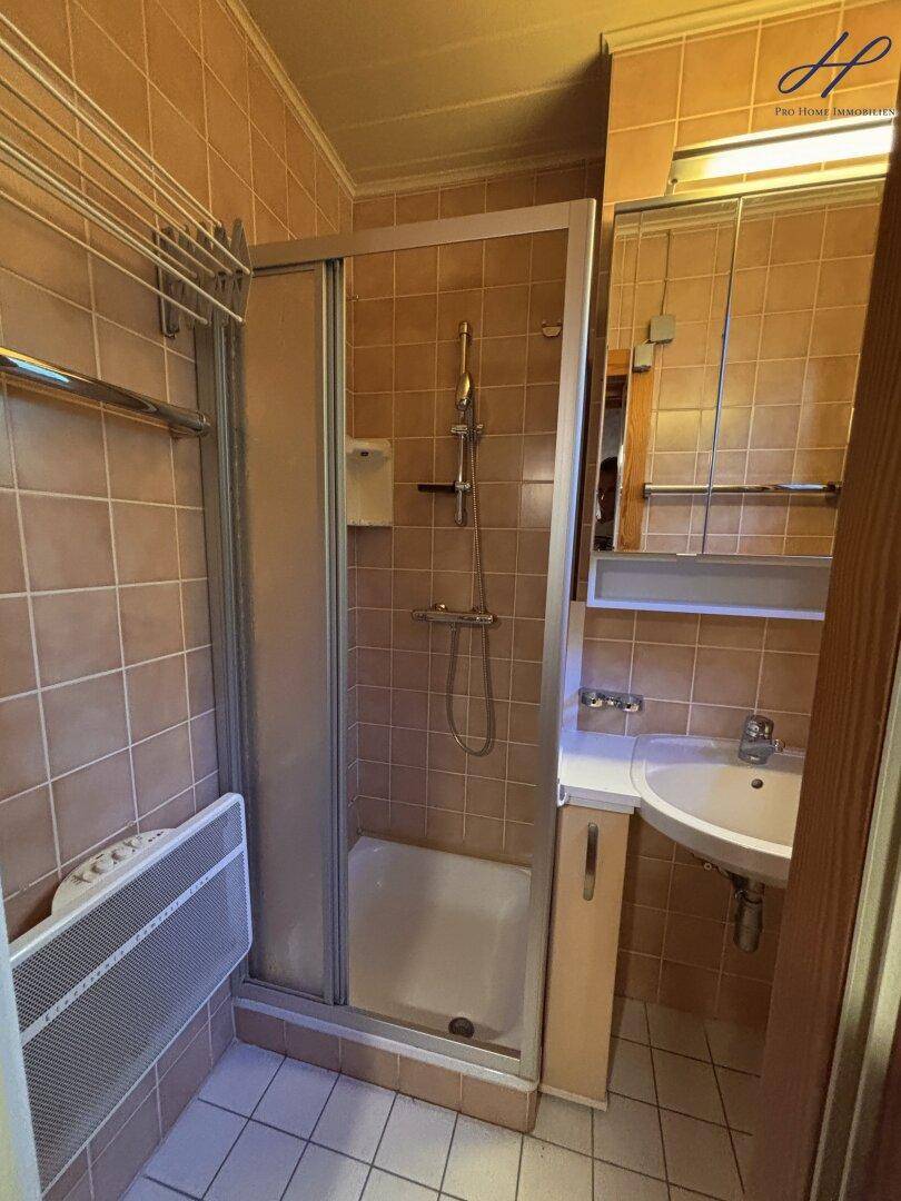 Badezimmer mit Duschkabine, Waschbecken und beigefarbenen Fliesen.