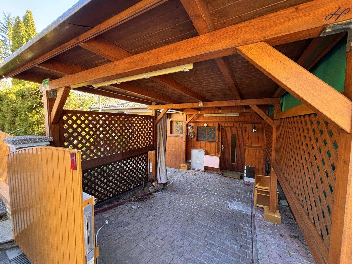 Überdachter Carport mit Holzkonstruktion und gepflastertem Boden.