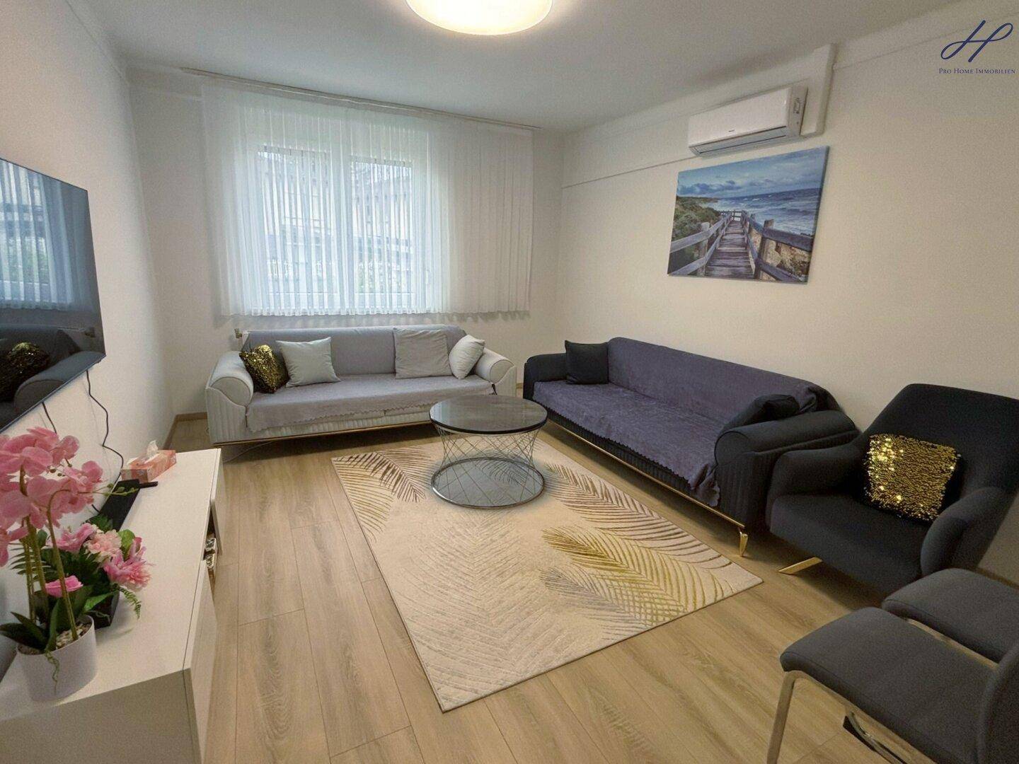 Helles Wohnzimmer mit Laminatboden, bequemen Sofas, einem Fernseher und Klimaanlage für Komfort.