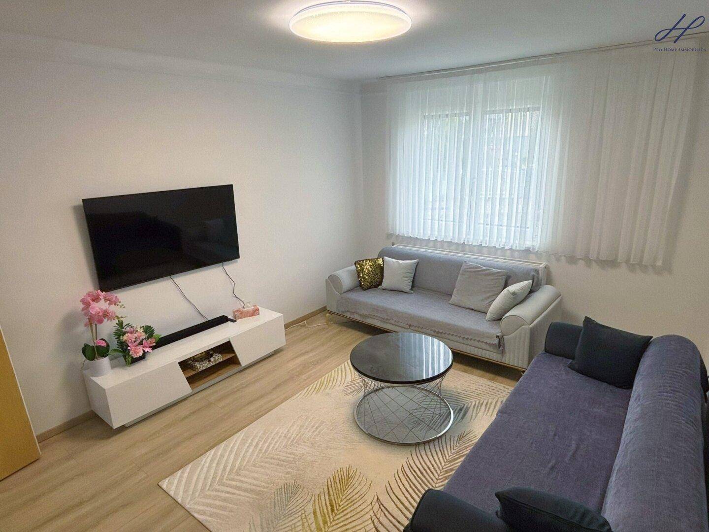 Geräumiges Wohnzimmer mit hellem Boden, modernen Möbeln und einem großen Fenster für viel Tageslicht.