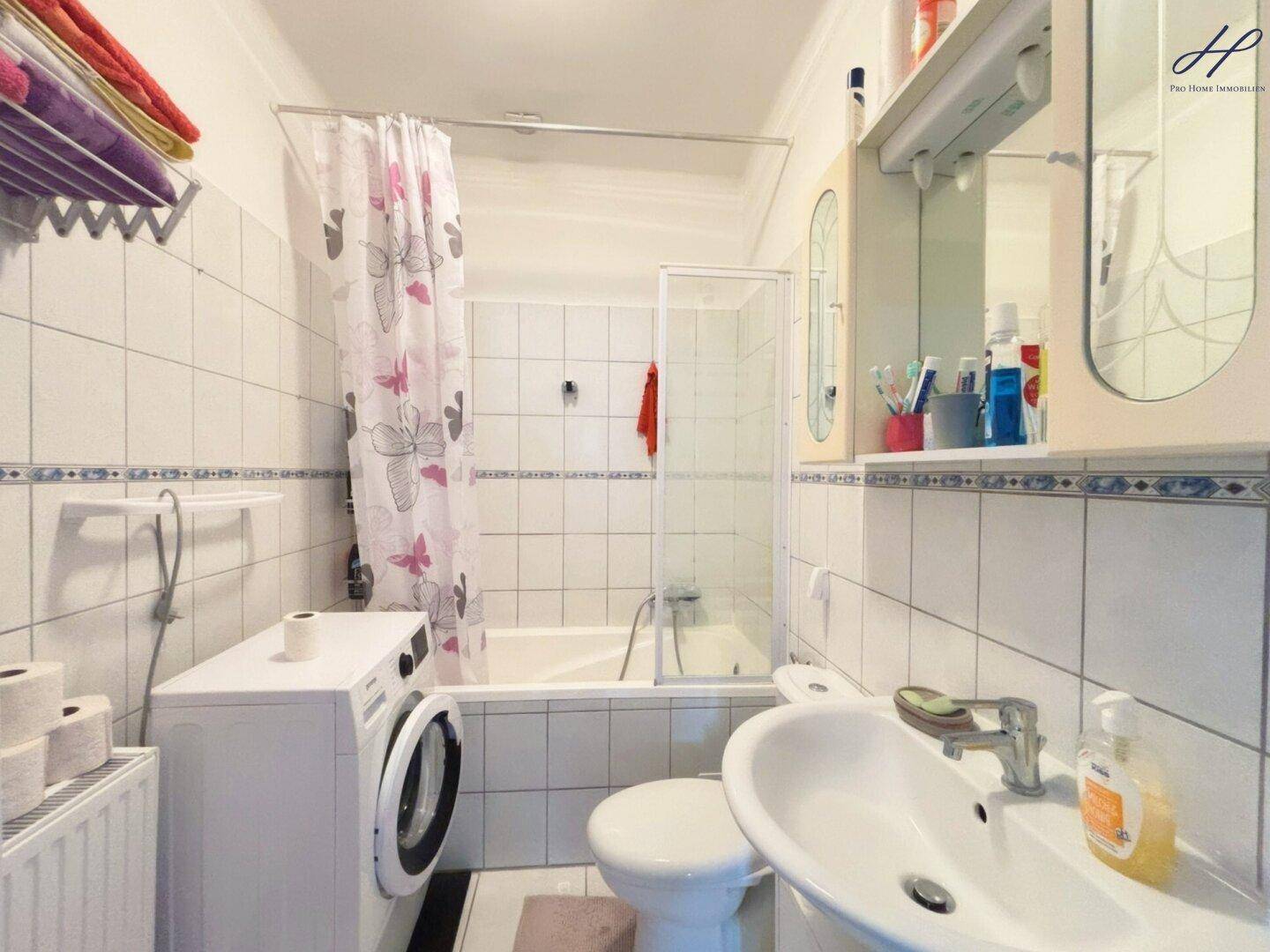 Funktionales Badezimmer mit Badewanne, Dusche, Waschbecken und Waschmaschine, komplett gefliest.