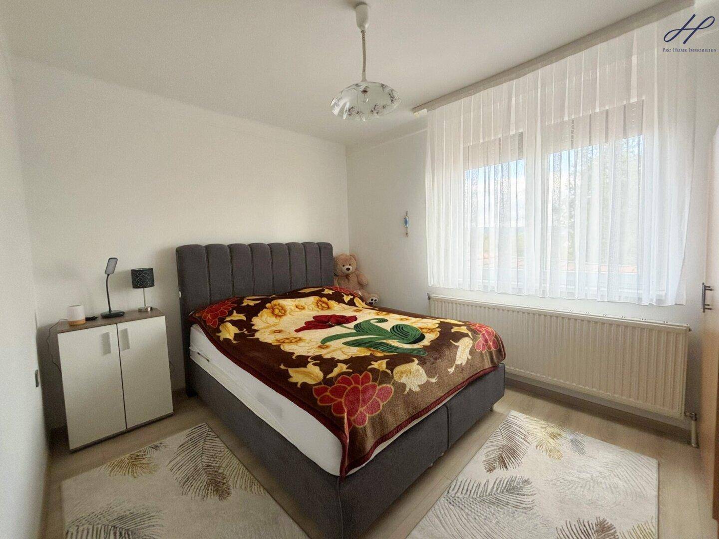 Gemütliches Schlafzimmer mit Doppelbett, Teppich und Fenster, das viel Tageslicht hereinlässt.