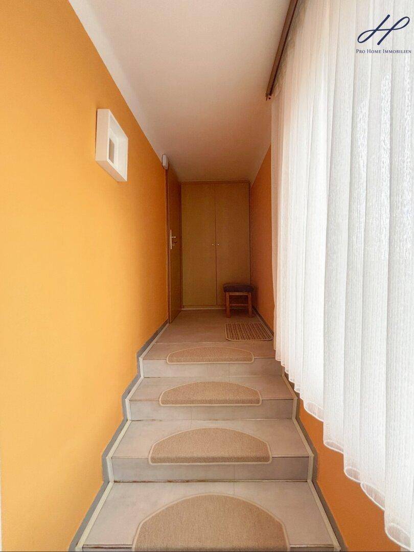 Treppenaufgang mit orangefarbenen Wänden und Teppichstufen, der zu den oberen Etagen führt.