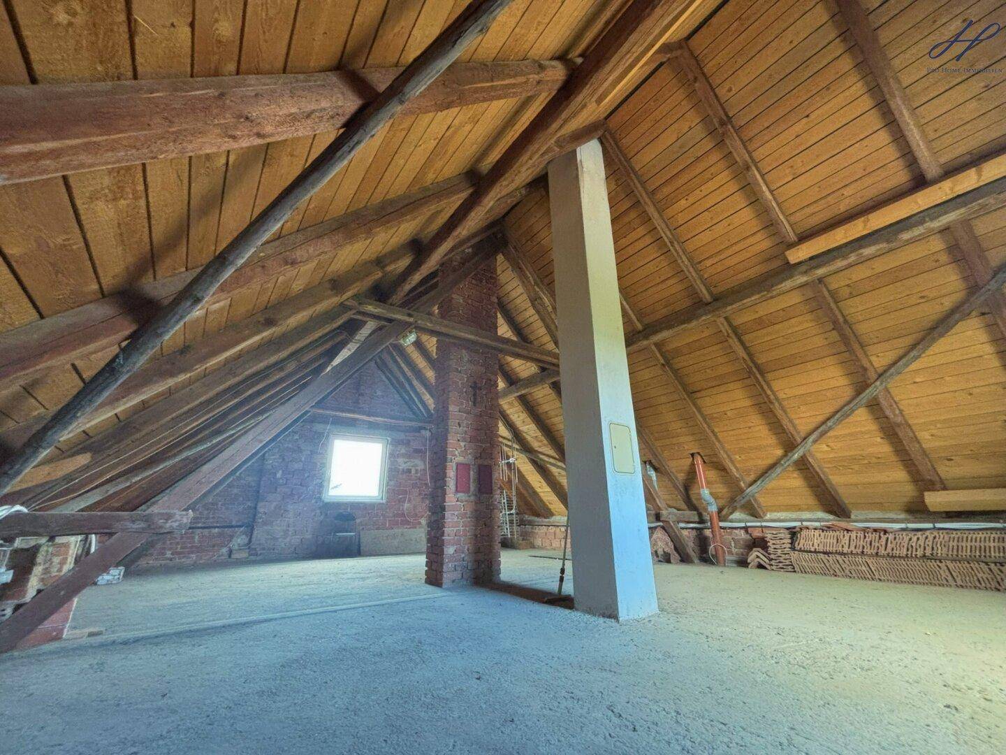 Geräumiger Dachboden mit sichtbaren Holzbalken und einem kleinen Fenster, bereit für Ausbau.