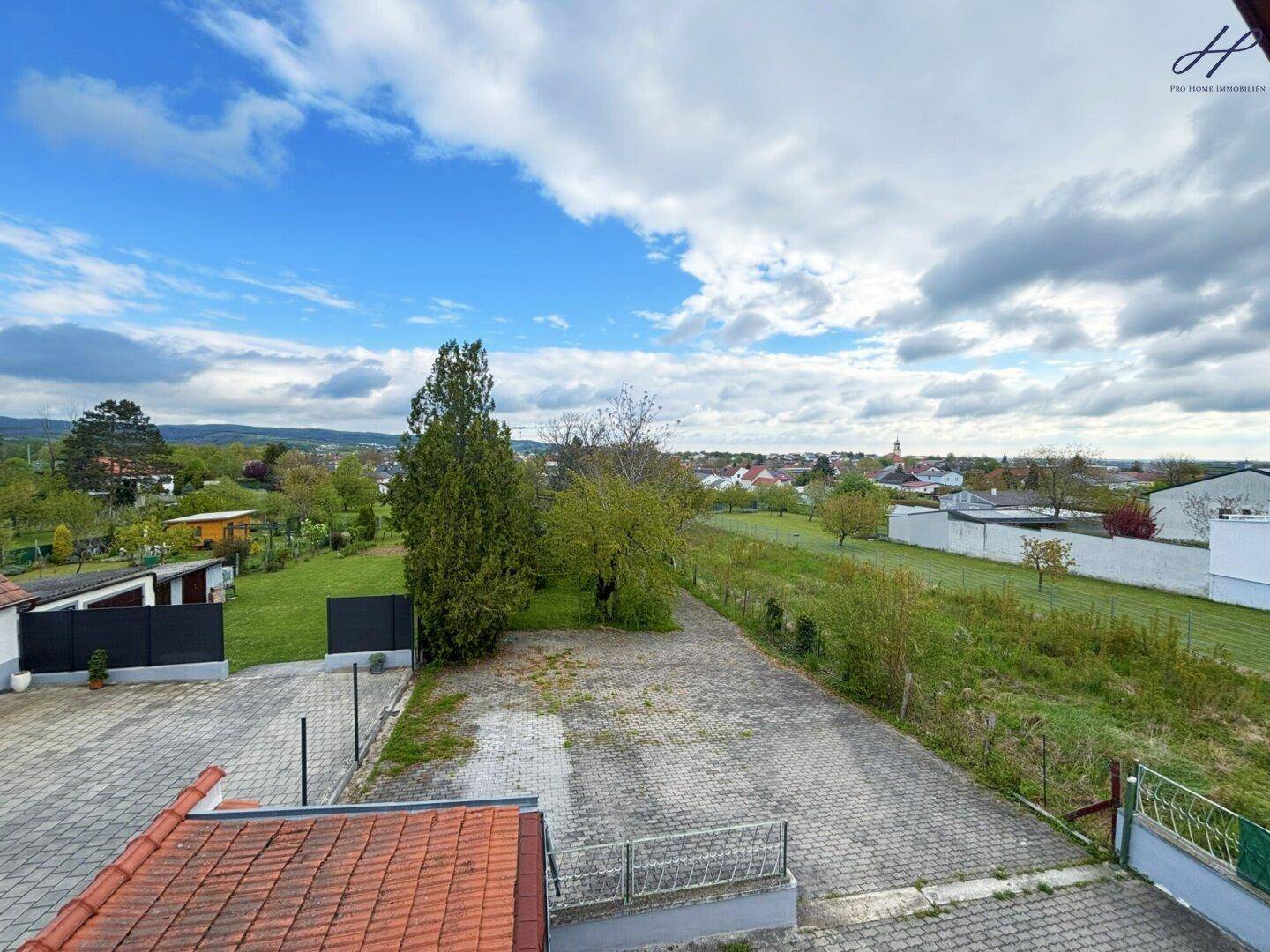 Weitläufiger Blick über die Umgebung mit viel Grün, Häusern und einem Dorf in der Ferne.