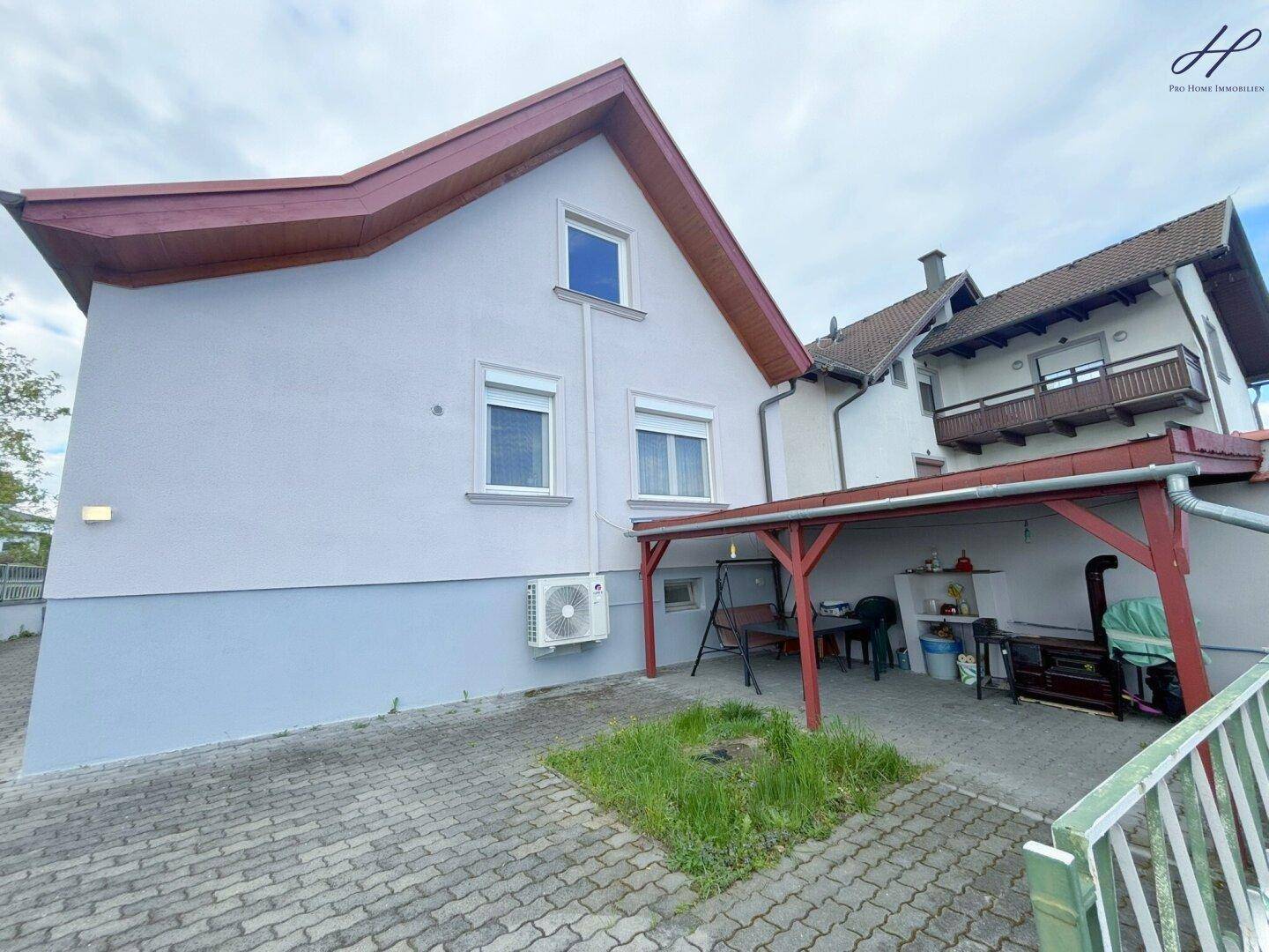 Rückansicht des Hauses mit überdachtem Terrassenbereich und gepflasterter Fläche, umgeben von Grün.