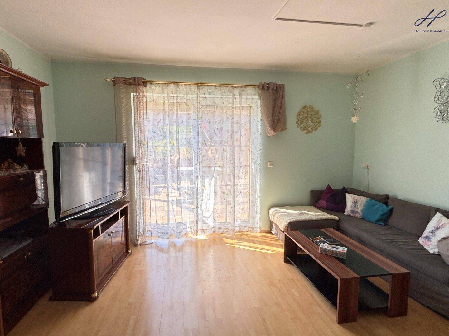 Gemütliches Wohnzimmer mit Holzboden, Sofa und großem Fenster zum Garten.