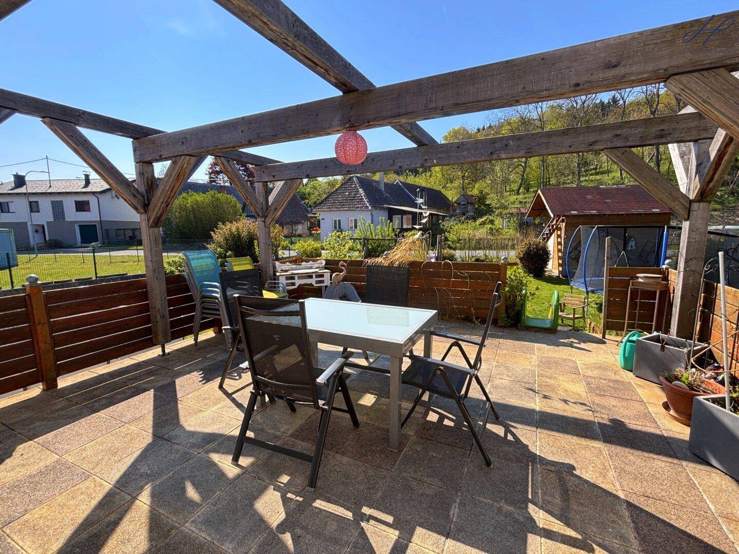 Sonniger Terrassenbereich mit Pergola, Gartenmöbeln und Blick ins Grüne.