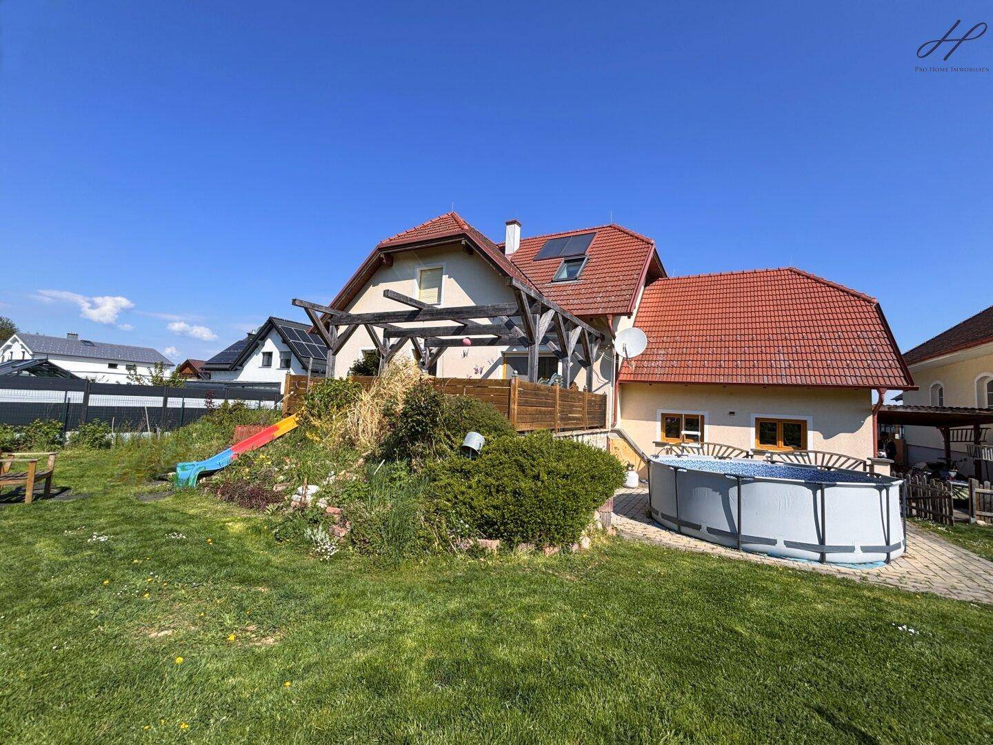 Weitläufiger Garten mit Aufstellpool, Rutsche und viel Grünfläche.