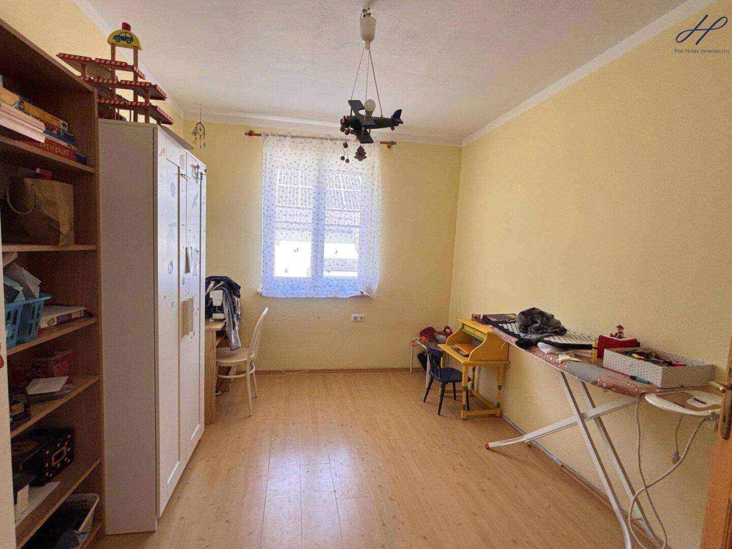 Kinderzimmer mit Laminatboden, Schreibtisch und hellem Fenster.
