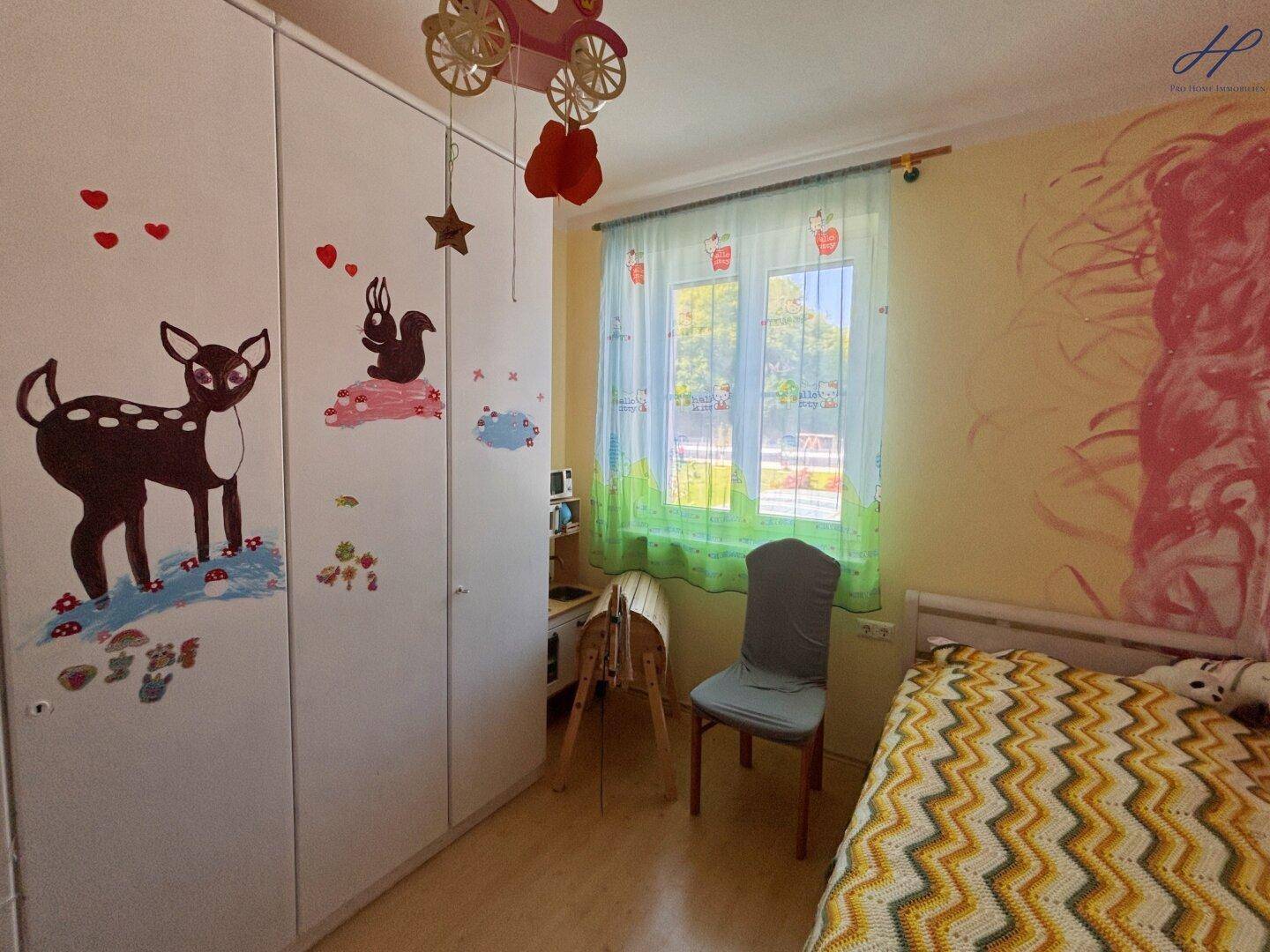 Buntes Kinderzimmer mit Laminatboden, Kleiderschrank und Fenster mit Blick ins Grüne.