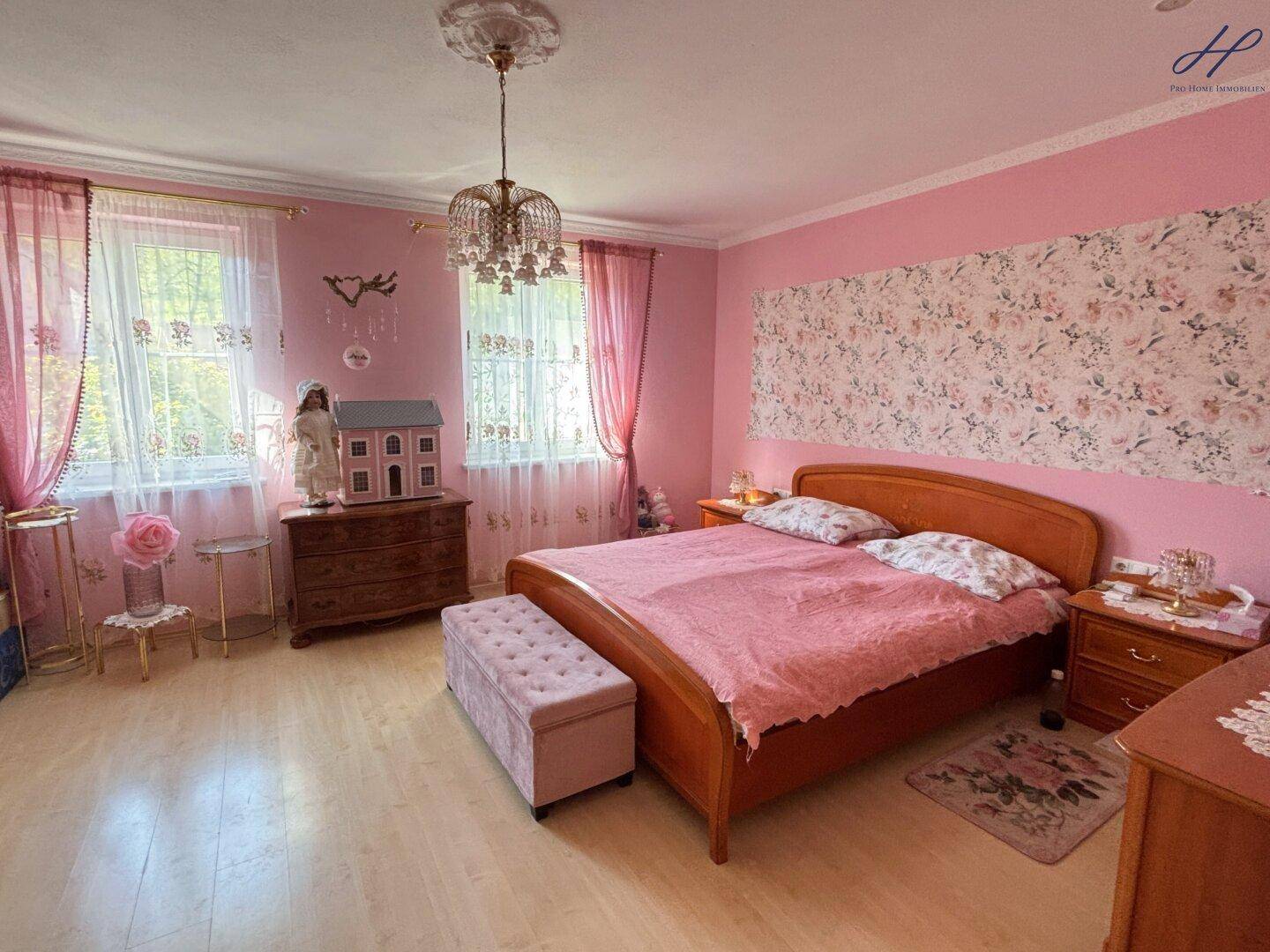 Romantisches Schlafzimmer in Rosa mit Doppelbett, Holzboden und Stuckdecke.