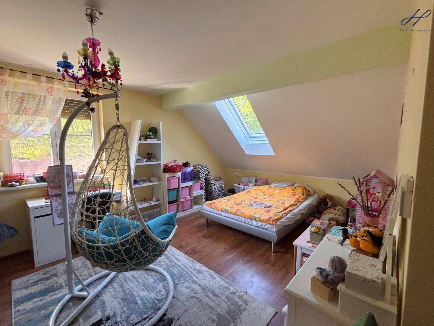 Helles Kinderzimmer im Dachgeschoss mit Schaukelstuhl, Bett und Dachfenster.