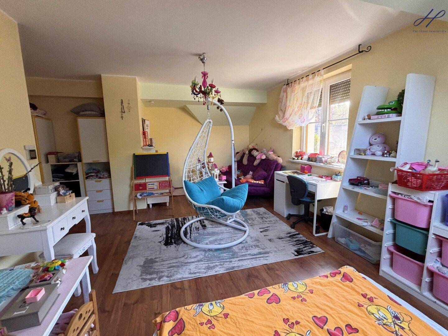 Geräumiges Kinderzimmer im Dachgeschoss mit Schaukelstuhl, Regalen und viel Stauraum.