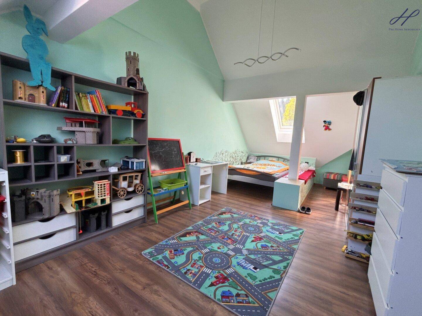 Helles Kinderzimmer mit Spielteppich, vielen Regalen und Dachfenster für natürliches Licht.