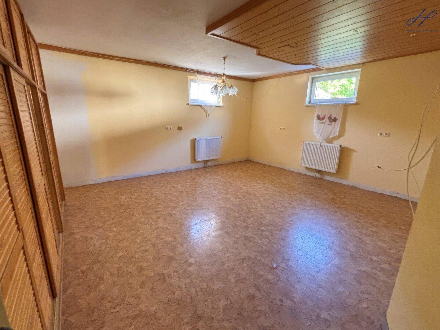 Leerer Raum mit hellen Wänden, zwei Fenstern, Heizkörpern und Holzpaneeldecke, bereit zur Gestaltung.