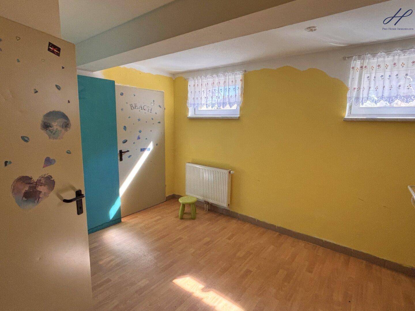 Heller Raum mit gelben Wänden, zwei Fenstern mit Vorhängen und Holzboden, ideal für ein Kinderzimmer.