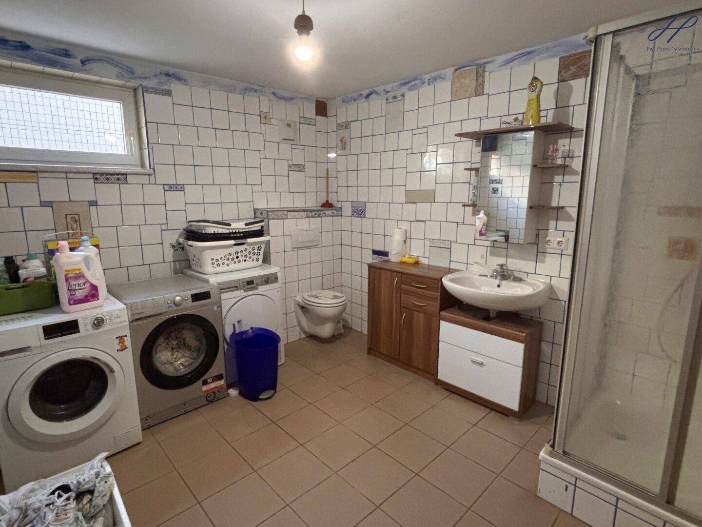 Funktionales Badezimmer mit Fliesen, Dusche, WC, Waschmaschine und Trockner sowie einem Fenster.