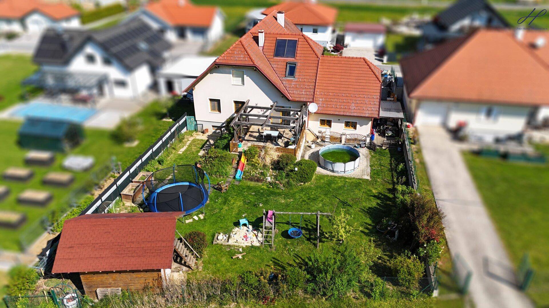 Luftaufnahme eines Hauses mit großem Garten, Trampolin, Pool, Gartenhaus und Terrasse.