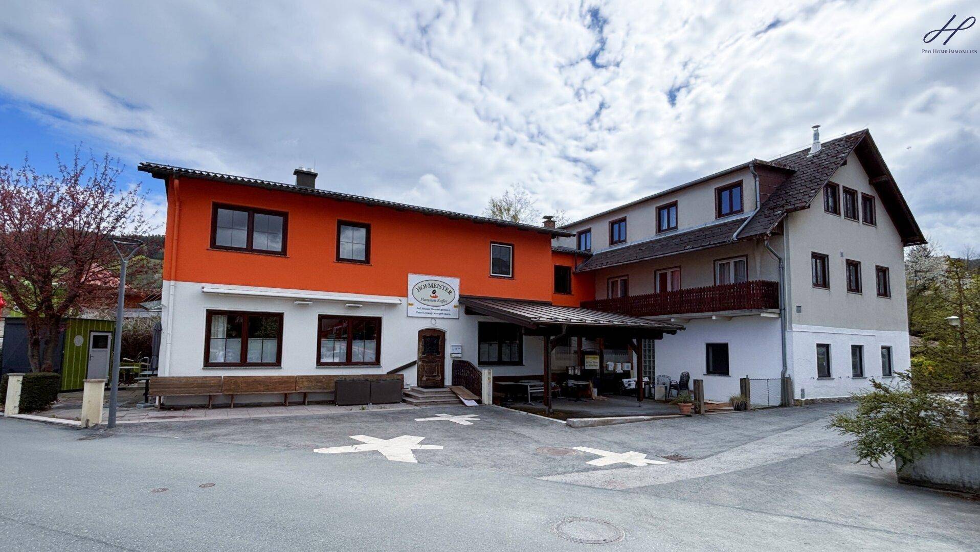 Mehrstöckiges Gebäude mit orangefarbener und weißer Fassade, umgeben von Bäumen und einem Parkplatz.
