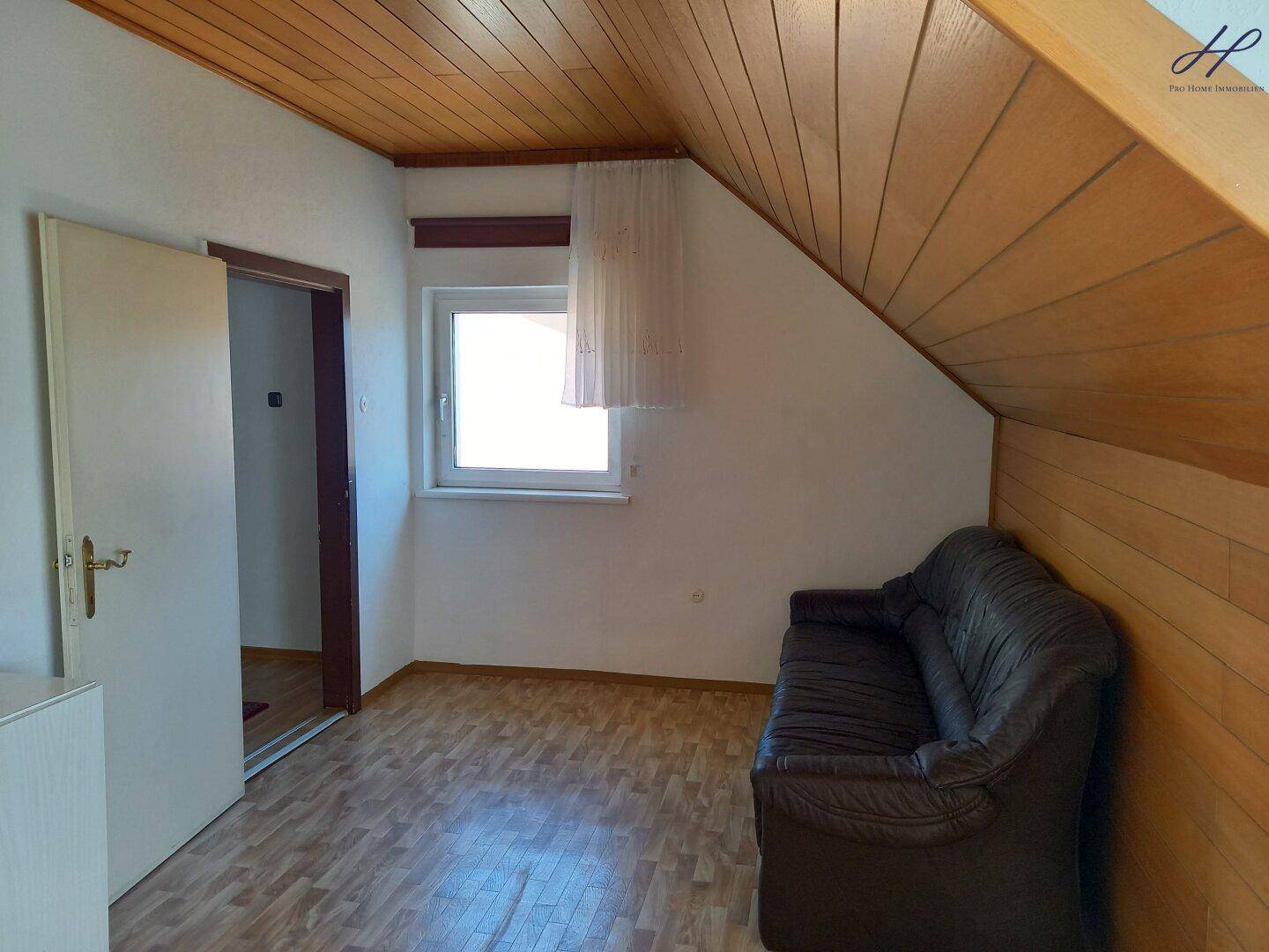 Helles Dachgeschosszimmer mit Schräge, Holzverkleidung und bequemer Couch.