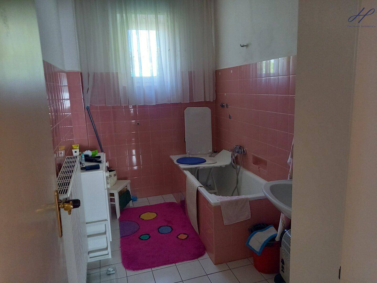 Badezimmer mit rosa Fliesen, Badewanne, Waschbecken und Fenster.