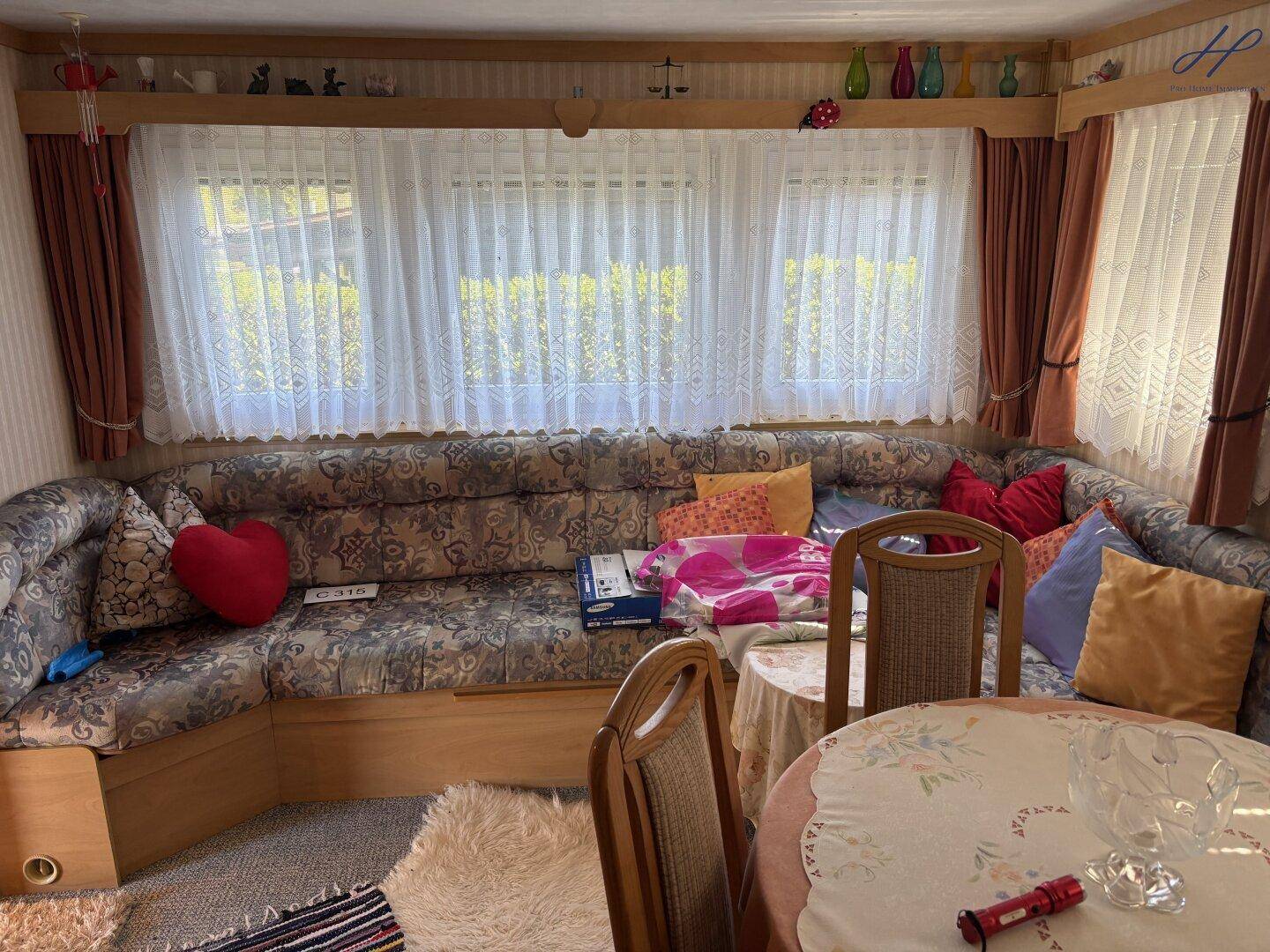 Wohnzimmer mit großer Eckcouch, vielen Kissen und breiten Fenstern für viel Tageslicht.