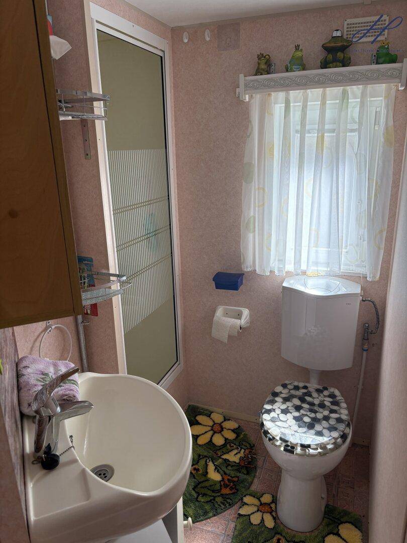 Kleines Badezimmer mit Waschbecken, Toilette und Duschkabine in rosa Farbtönen.