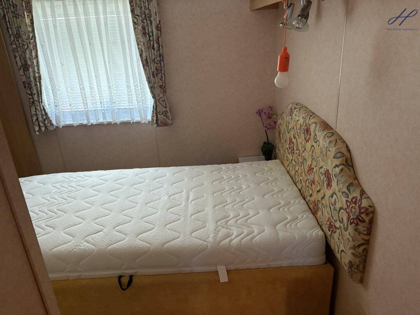 Gemütliches Schlafzimmer mit Bett, floralem Kopfteil und Fenster für natürliche Belichtung.
