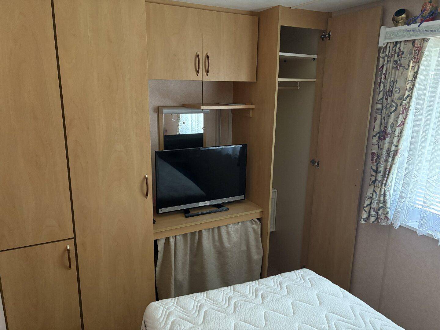 Schlafzimmer mit Einbauschränken aus hellem Holz und einem kleinen Fernseher.