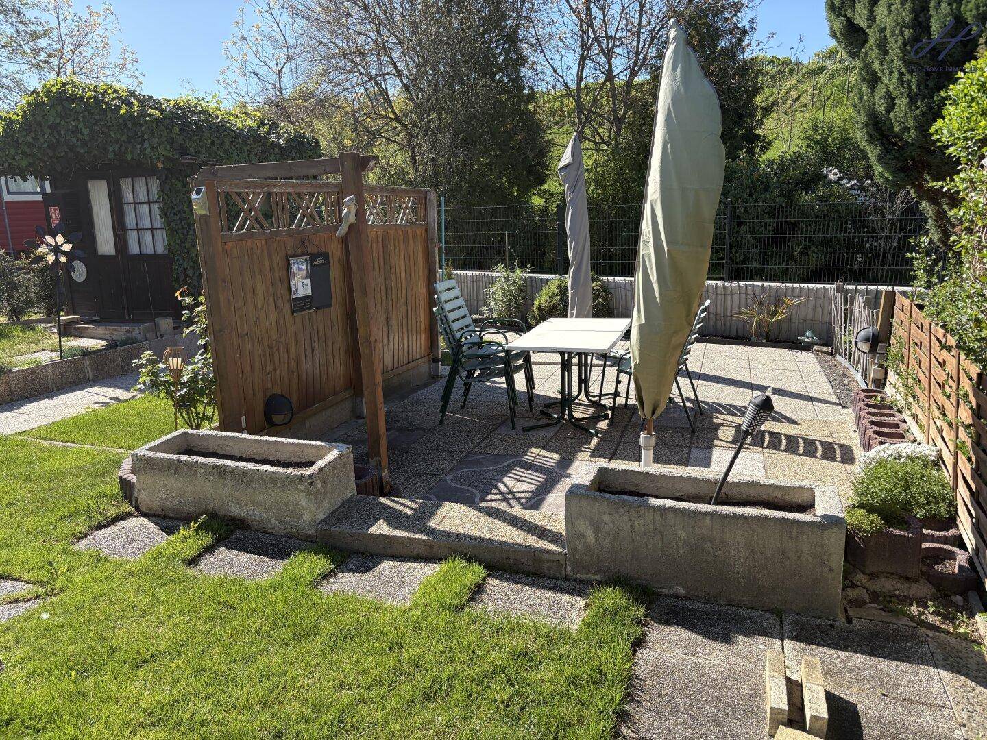 Sonniger Terrassenbereich mit Gartenmöbeln, Sonnenschirm und dekorativen Pflanzgefäßen.