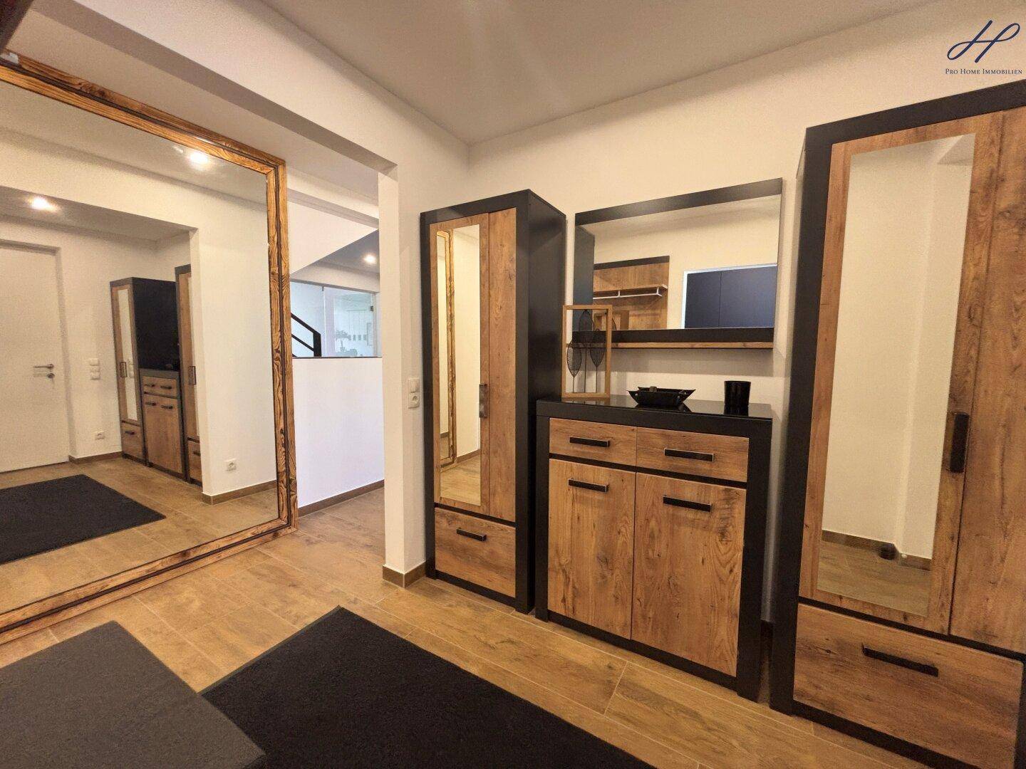 Heller Eingangsbereich mit Holzmöbeln, großem Spiegel und dunklem Teppich.