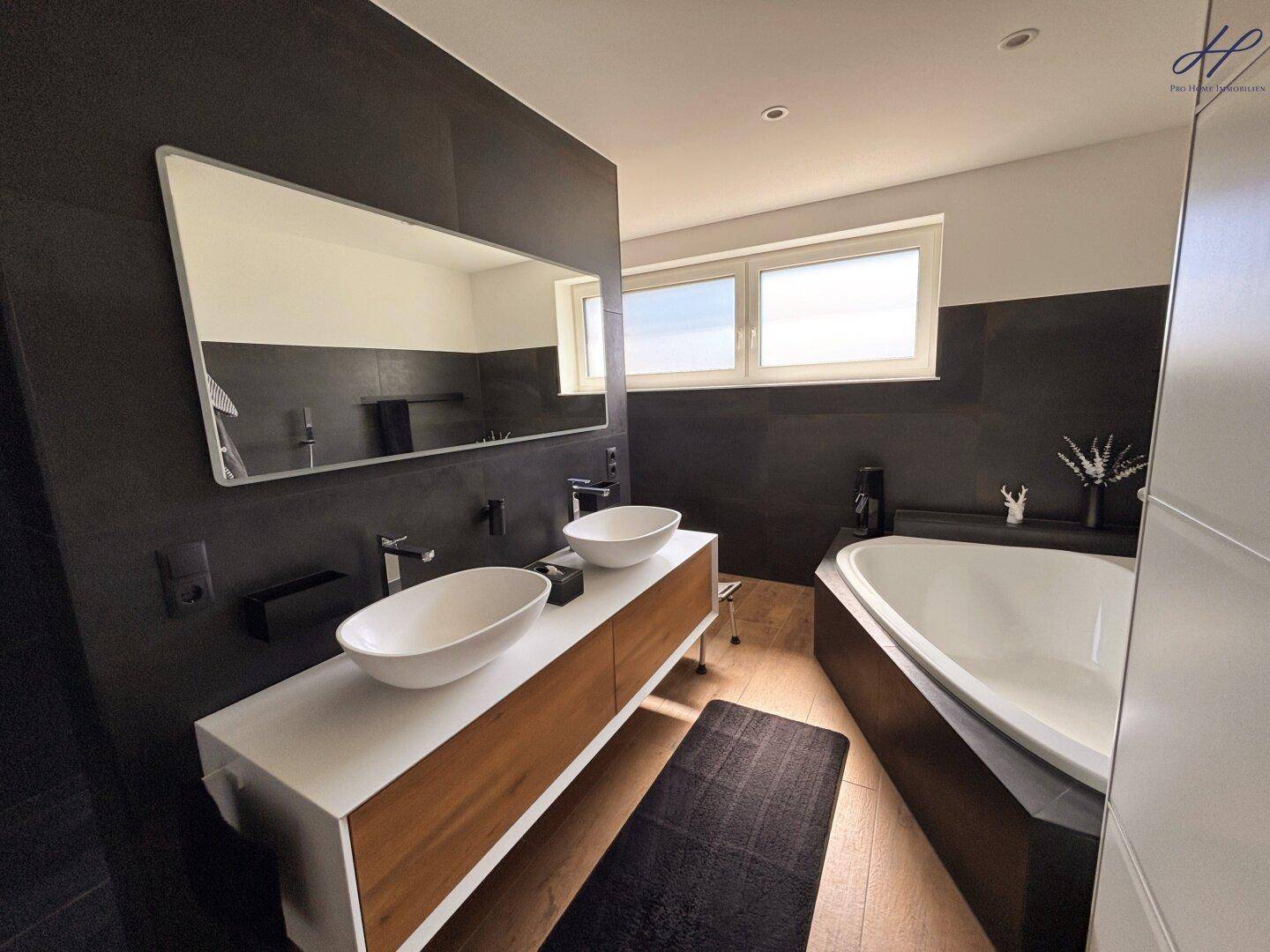 Modernes Badezimmer mit Doppelwaschbecken, Badewanne und dunklen Wandfliesen für ein elegantes Ambiente.