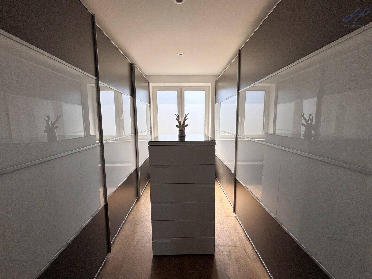 Begehbarer Kleiderschrank mit Einbauschränken und zentraler Kommode, ideal für Organisation.