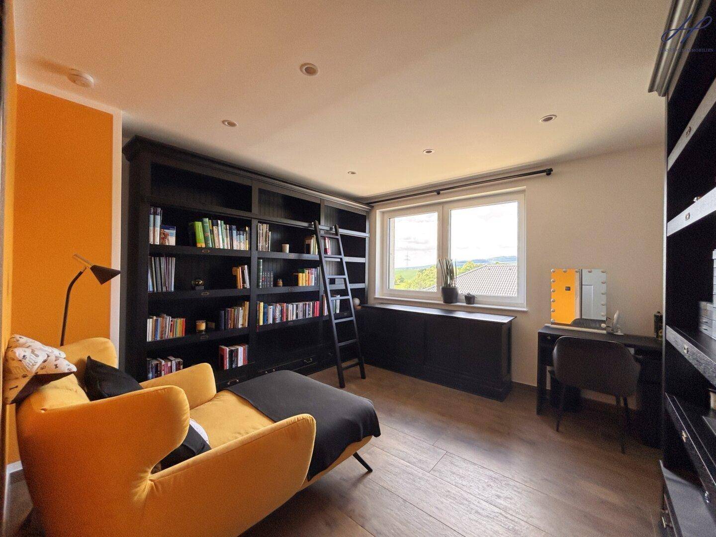 Gemütliches Arbeitszimmer mit Bücherregalen, Lesesessel und einem Fenster mit Blick ins Grüne.