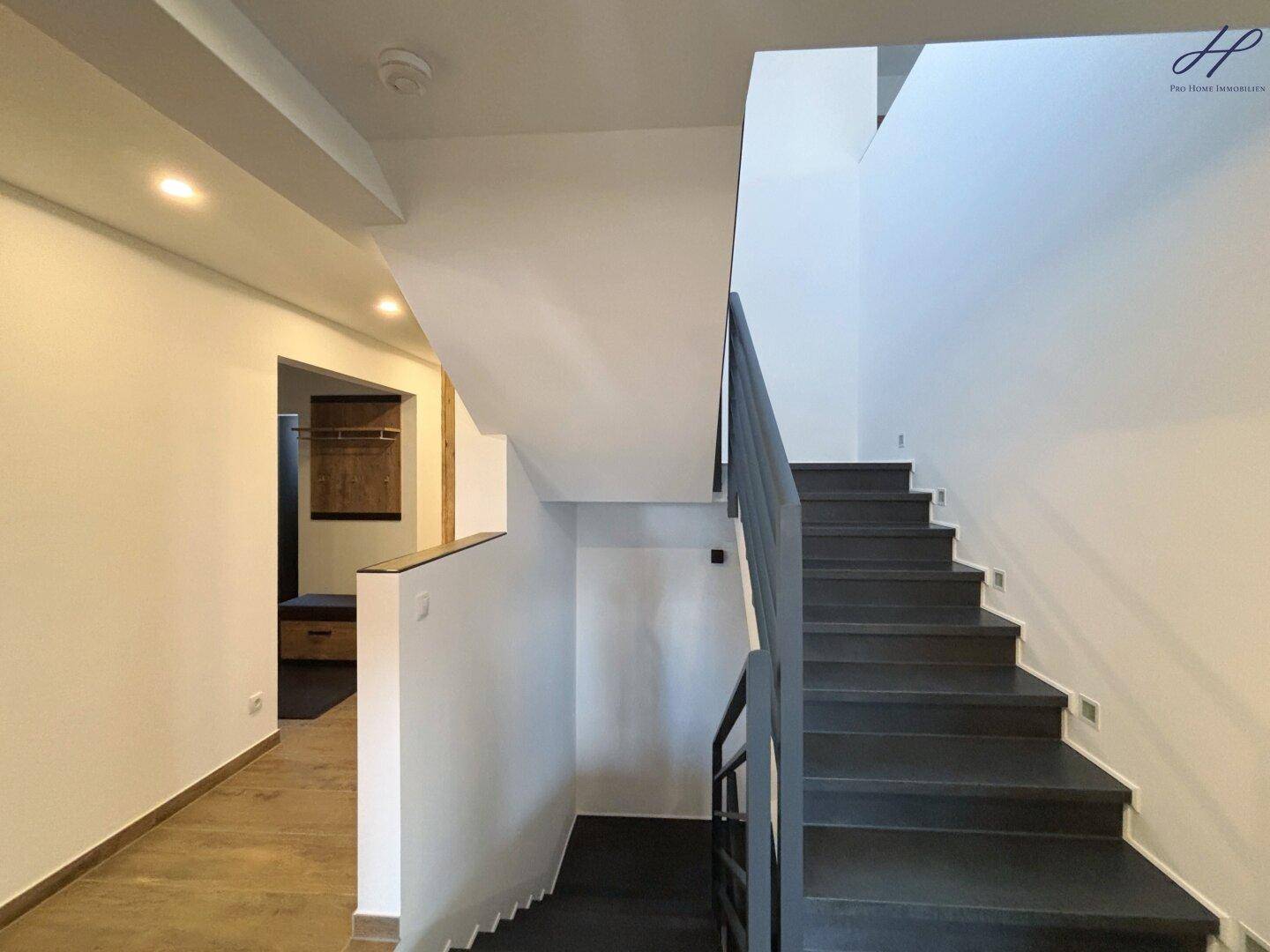 Heller Treppenaufgang mit modernem Design und Blick auf den Flur und die Garderobe.