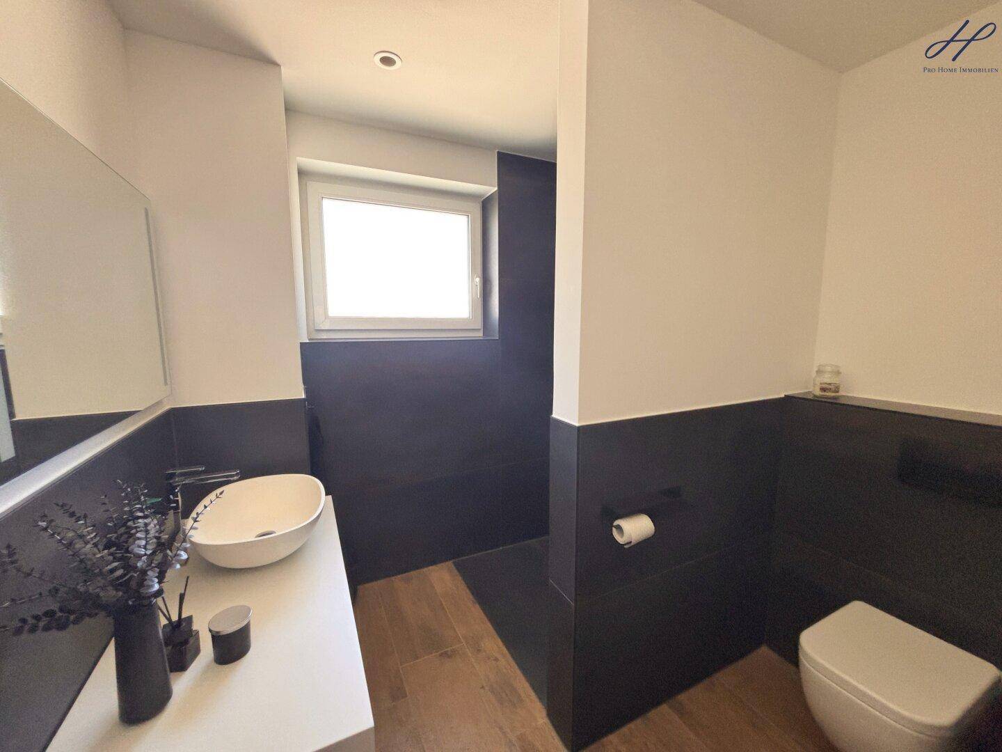 Modernes Badezimmer mit dunklen Fliesen, weißem Waschbecken und Fenster für Tageslicht.