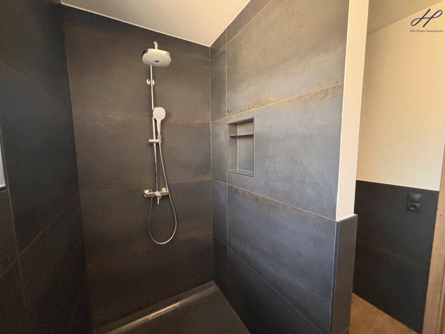 Geräumige Dusche mit dunklen Fliesen und moderner Armatur in einem stilvollen Badezimmer.