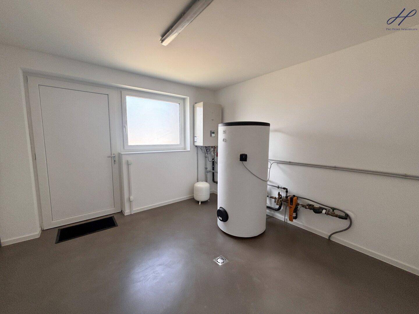 Technikraum mit Heizungsanlage, Warmwasserspeicher und Fenster für Belüftung und Tageslicht.