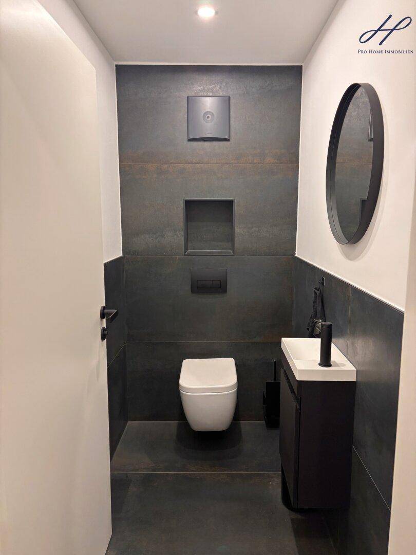 Modernes Gäste-WC mit Wand-WC, kleinem Waschbecken und dunklen Fliesen für ein stilvolles Design.