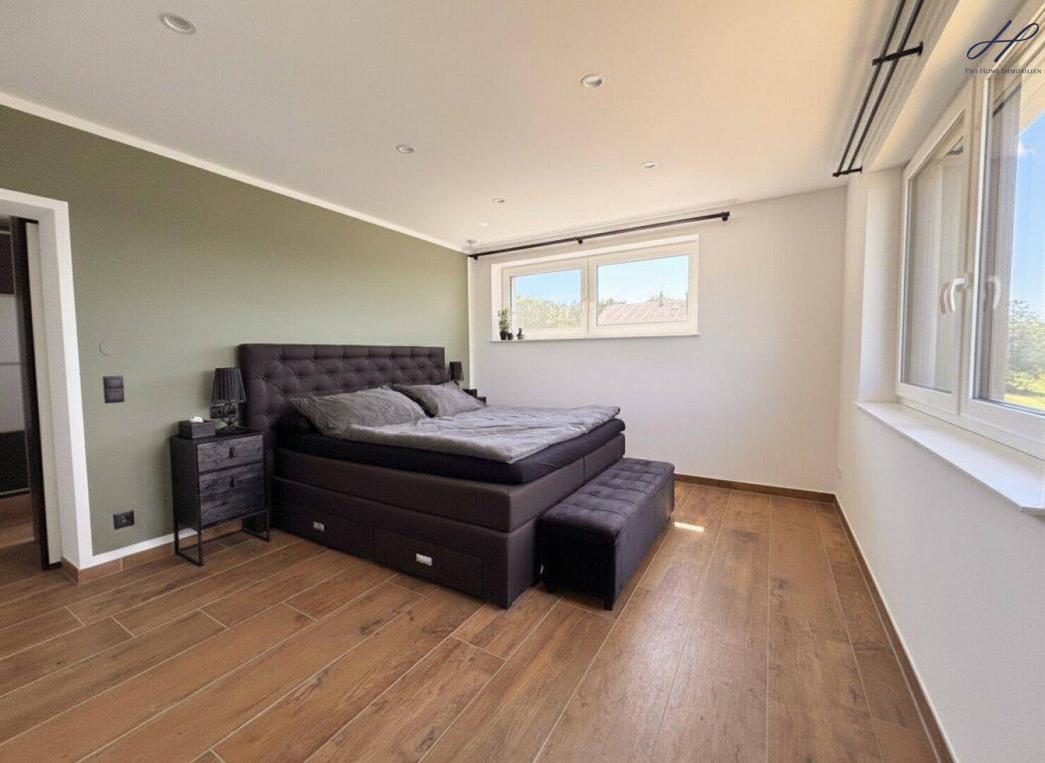 Helles Schlafzimmer mit großem Bett, Holzoptik-Boden und einer grünen Akzentwand für Gemütlichkeit.